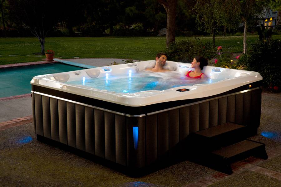Couple in huge hot tub in backyard that also has a pool